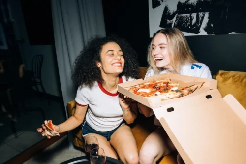 girls share a joke with wine and pizza