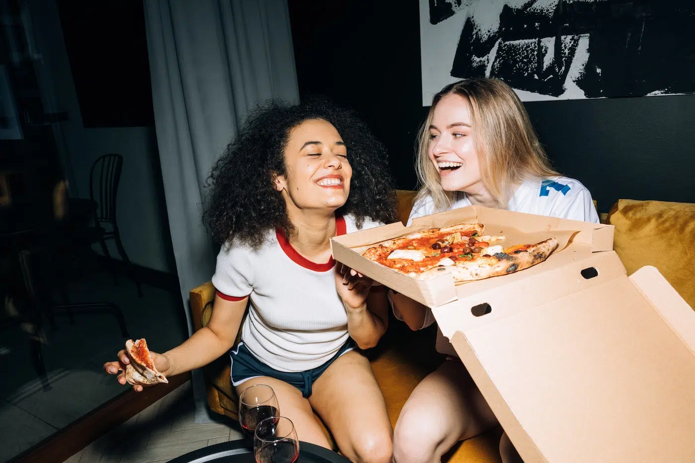 Girls share a joke with wine and pizza