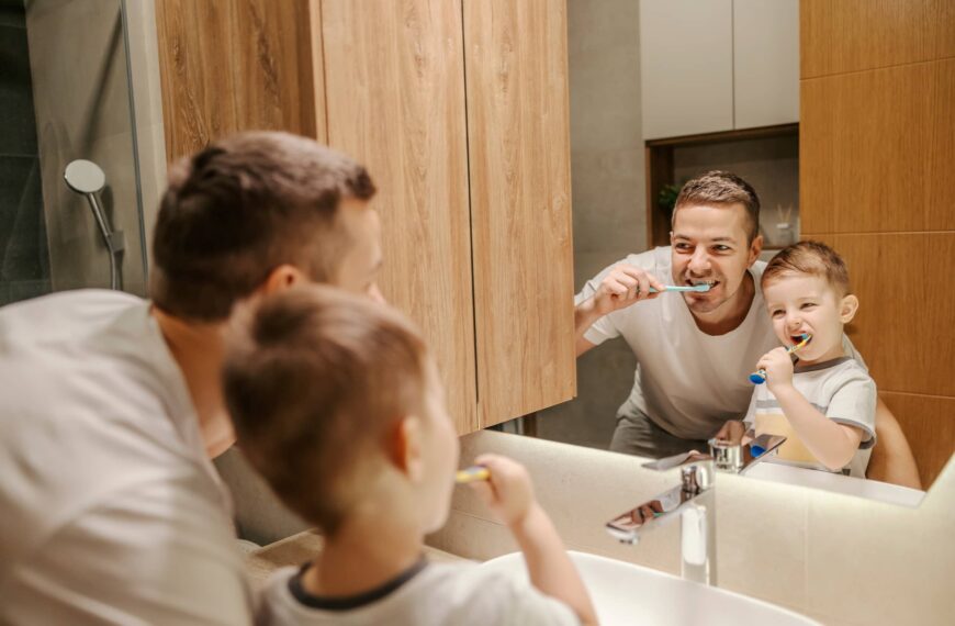 Reflection of a father and a little boy brushing their teeth in a bathroom.