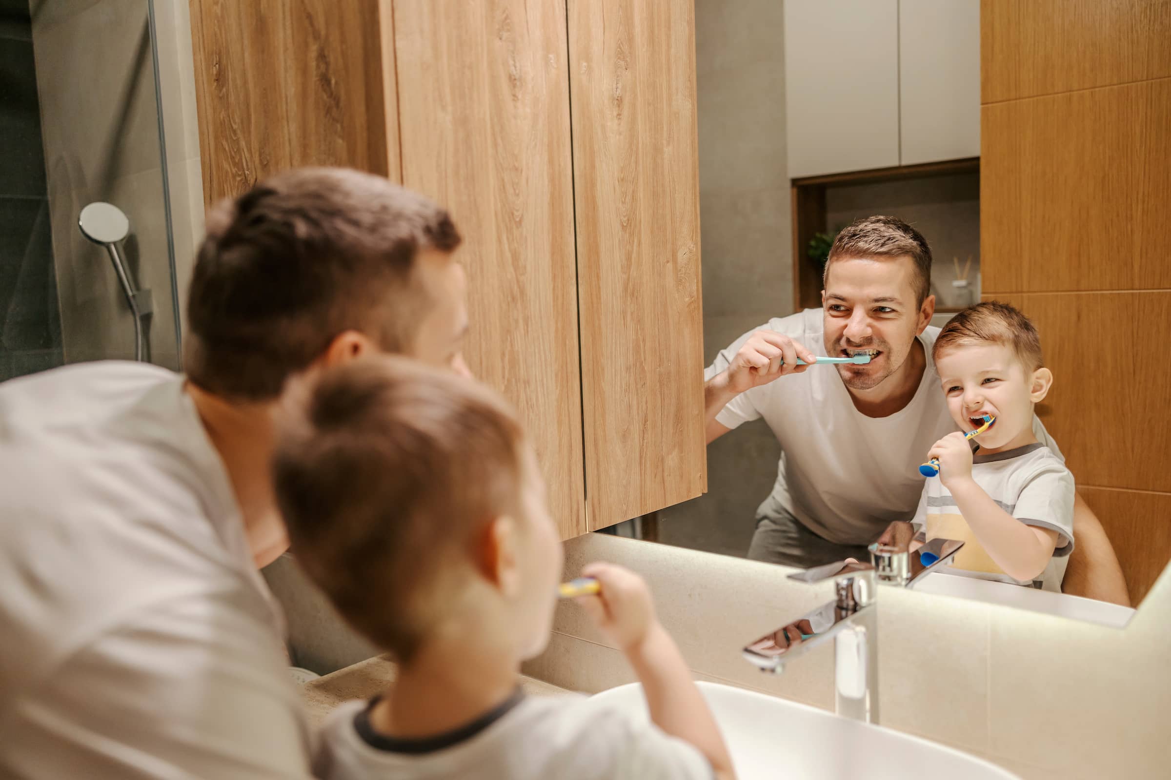 Reflection of a father and a little boy brushing their teeth in a bathroom.