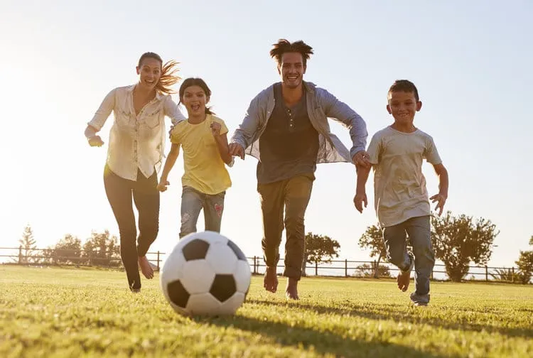 Young family chasing after a football in a park