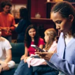 Person engrossed in phone, feeling alone among friends at social gathering