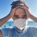 man holds head wearing facemask