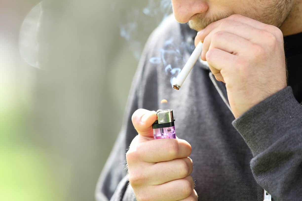 Close up of a teen hands holding a lighter lighting a cigarette ready to smoke
