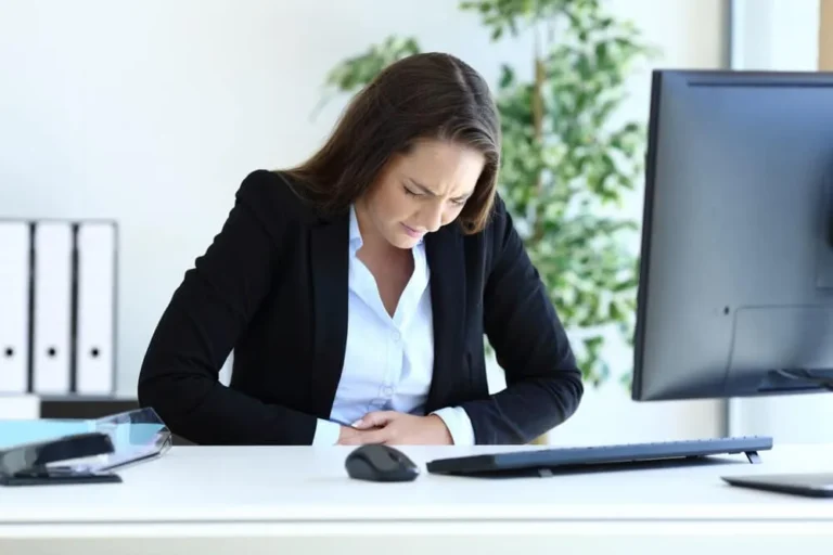 woman at desk holds stomach
