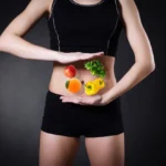 person in shorts and vest holds vegetables over stomach