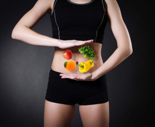 person in shorts and vest holds vegetables over stomach