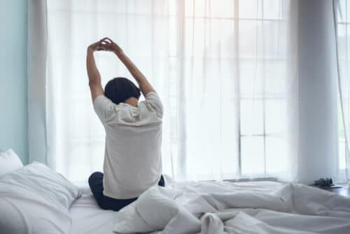 person stretches as they rise from bed e1612730636562