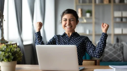 woman celebrates behind laptop scaled