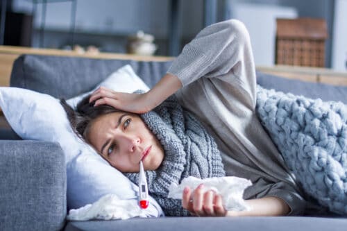 woman lays on sofa with thermometer in mouth