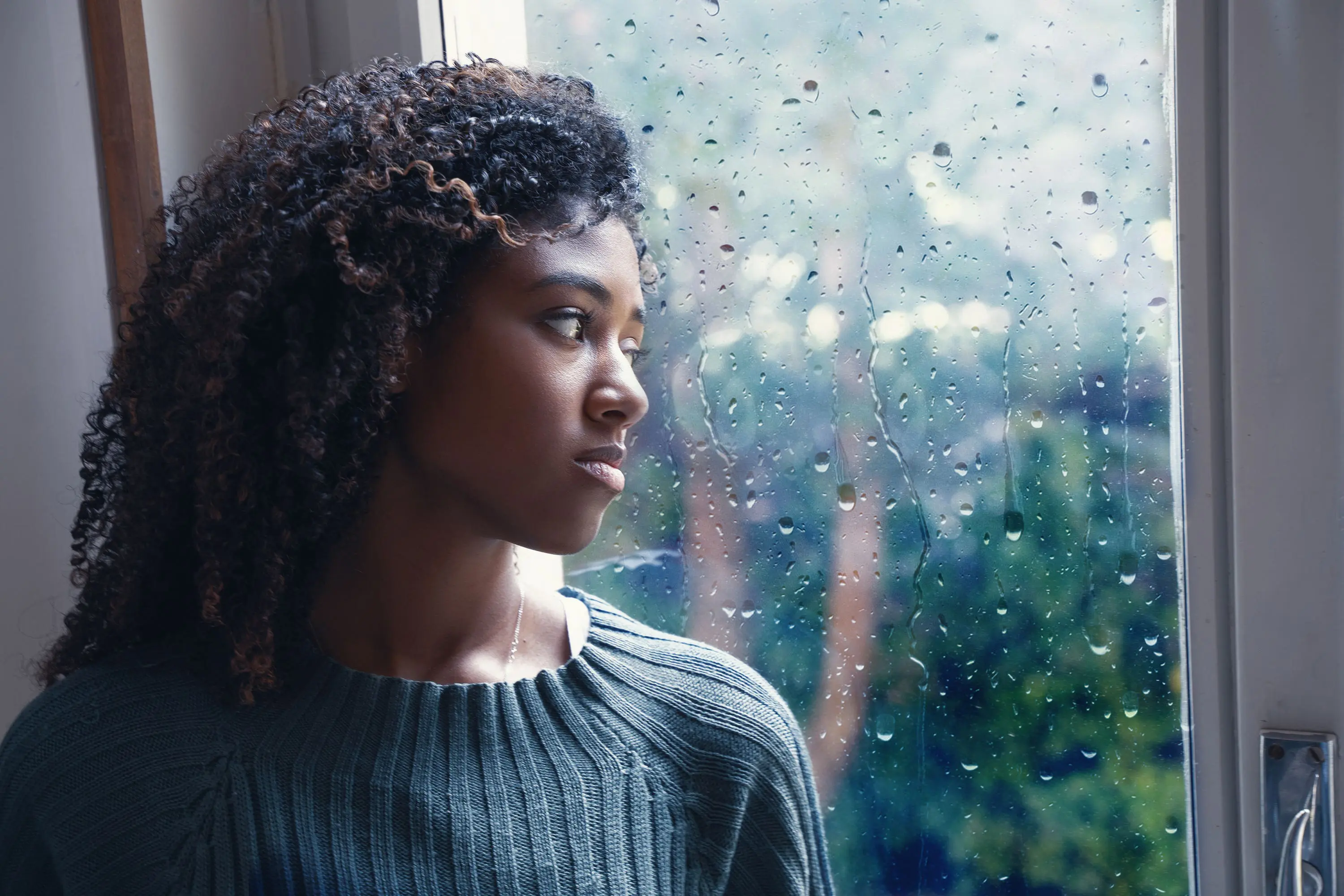 Woman looks sad by rainy window scaled