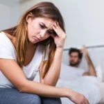 woman sits at end of bed looking stressed scaled