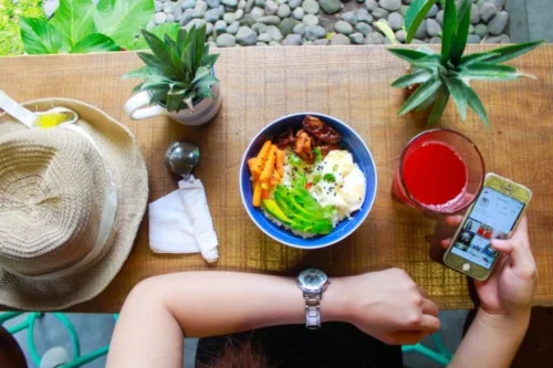 woman with phone in hand and food at table