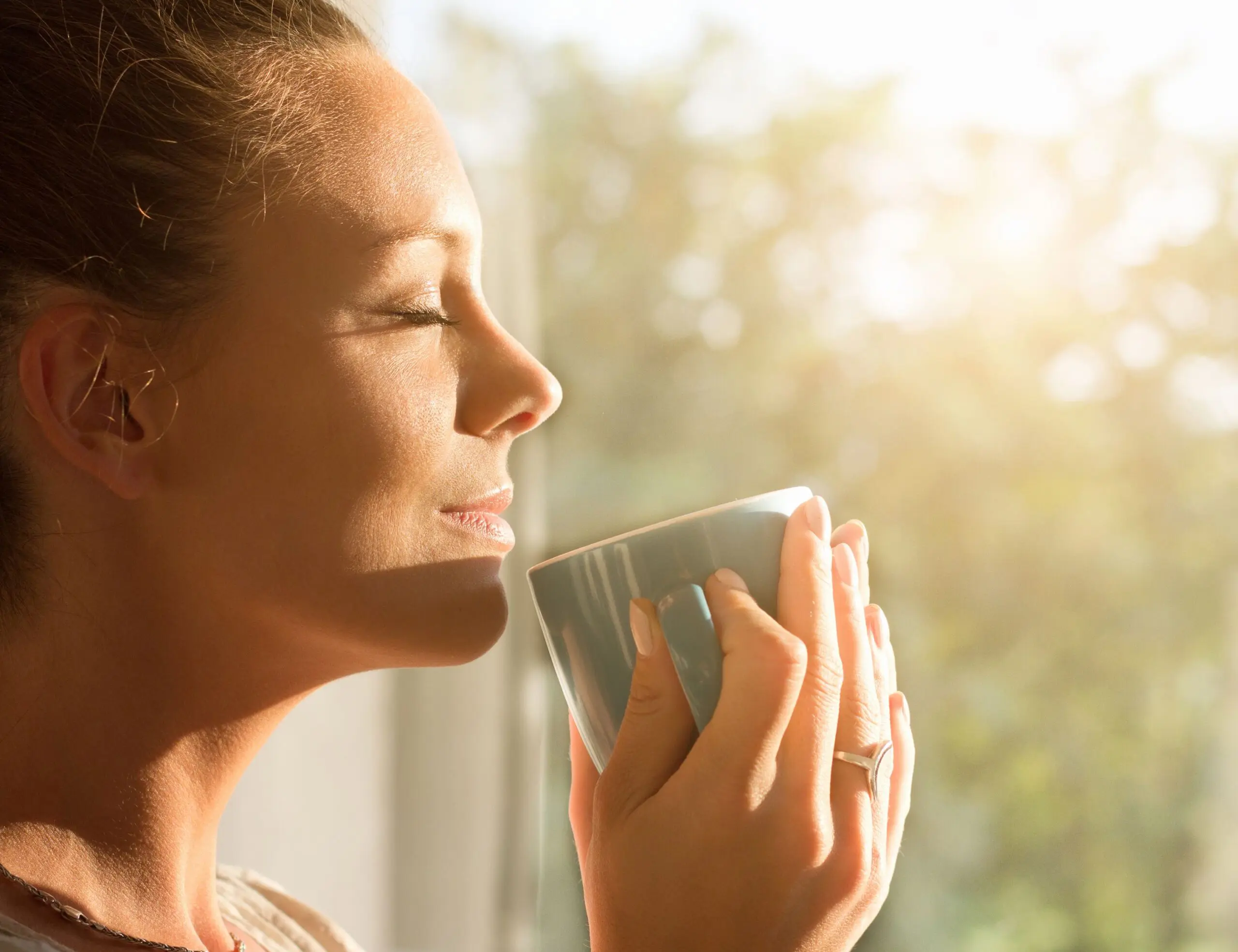 Woman holding cup smiles in the sunshine