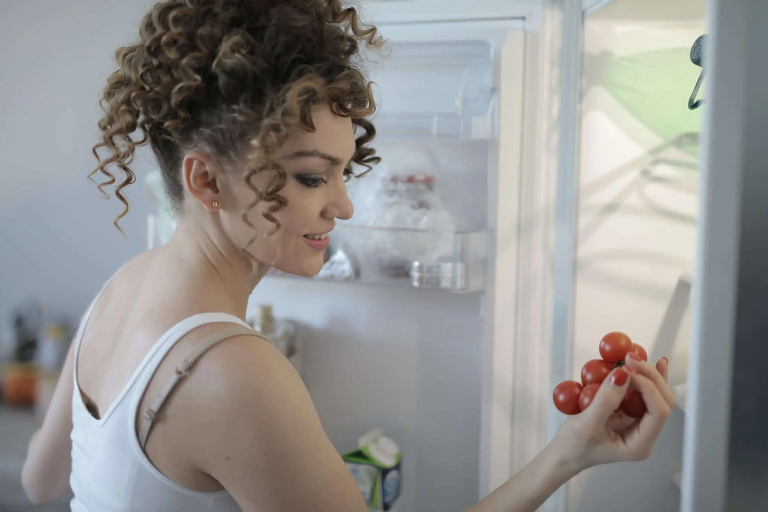 Woman looking at tomatoes in fridge scaled