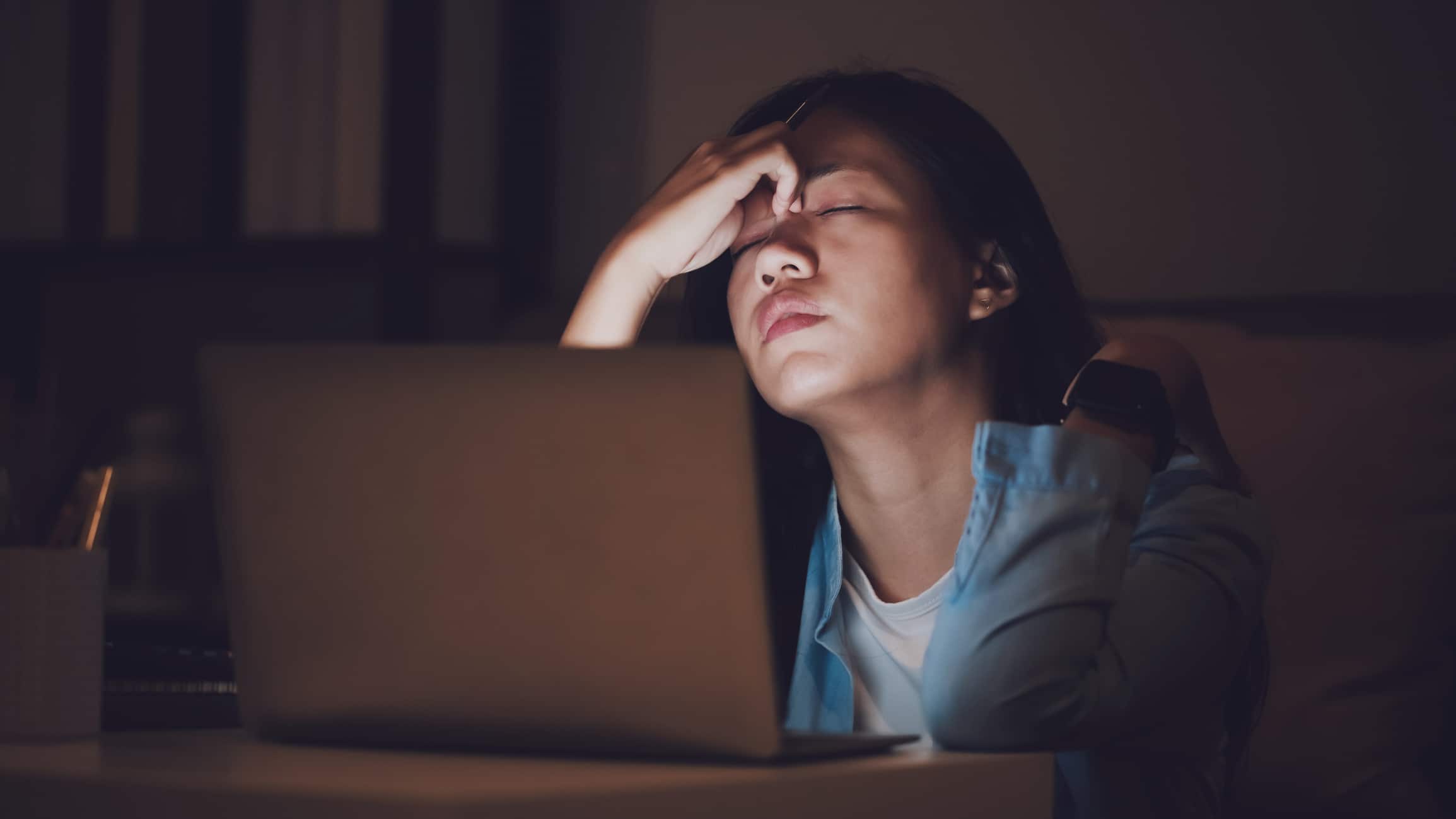 Asian woman student or businesswoman work late at night. Concentrated and feel sleepy at the desk in dark room with laptop or notebook. Concept of people workhard and burnout syndrome.