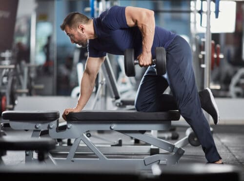 man lifts dumbbell over bench