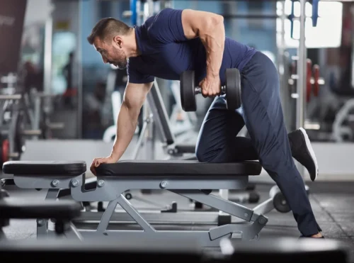 man lifts dumbbell over bench
