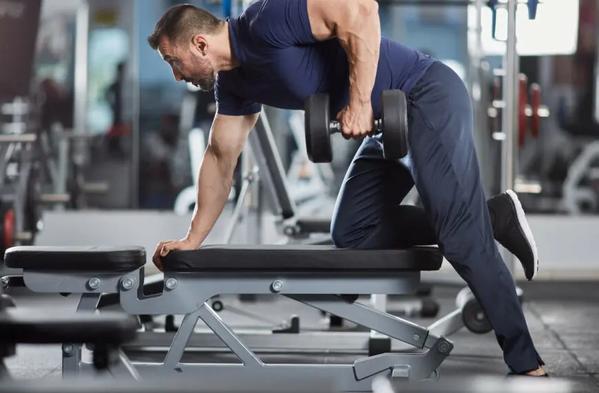 man lifts dumbbell over bench