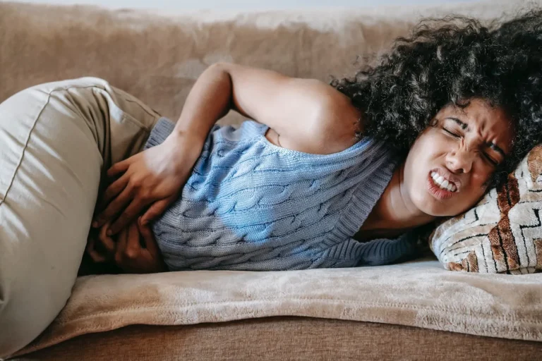 woman lays on couch holding stomach in pain
