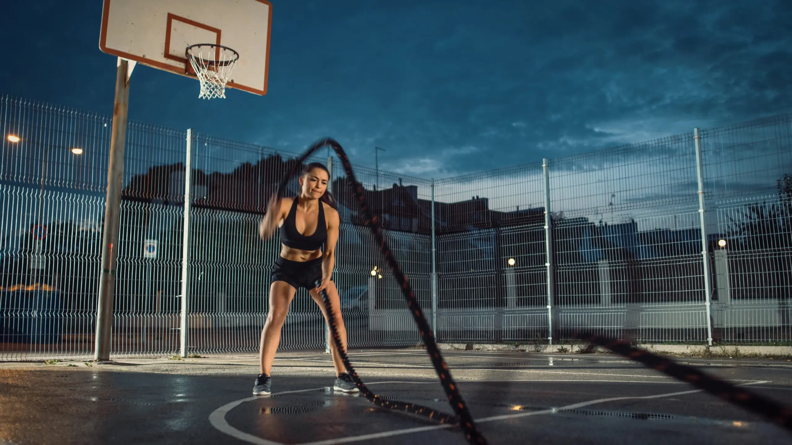 Fit girl using battle ropes on basketball court scaled