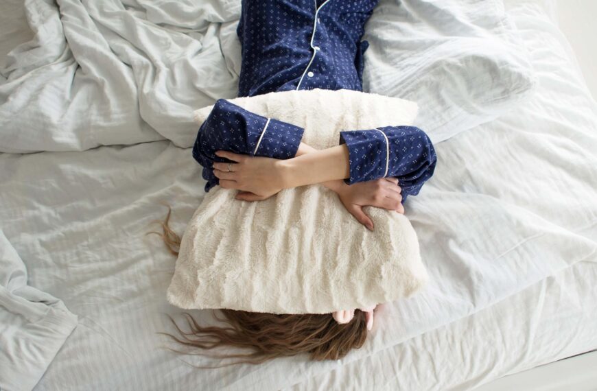 person lays on bed with pillow over face scaled