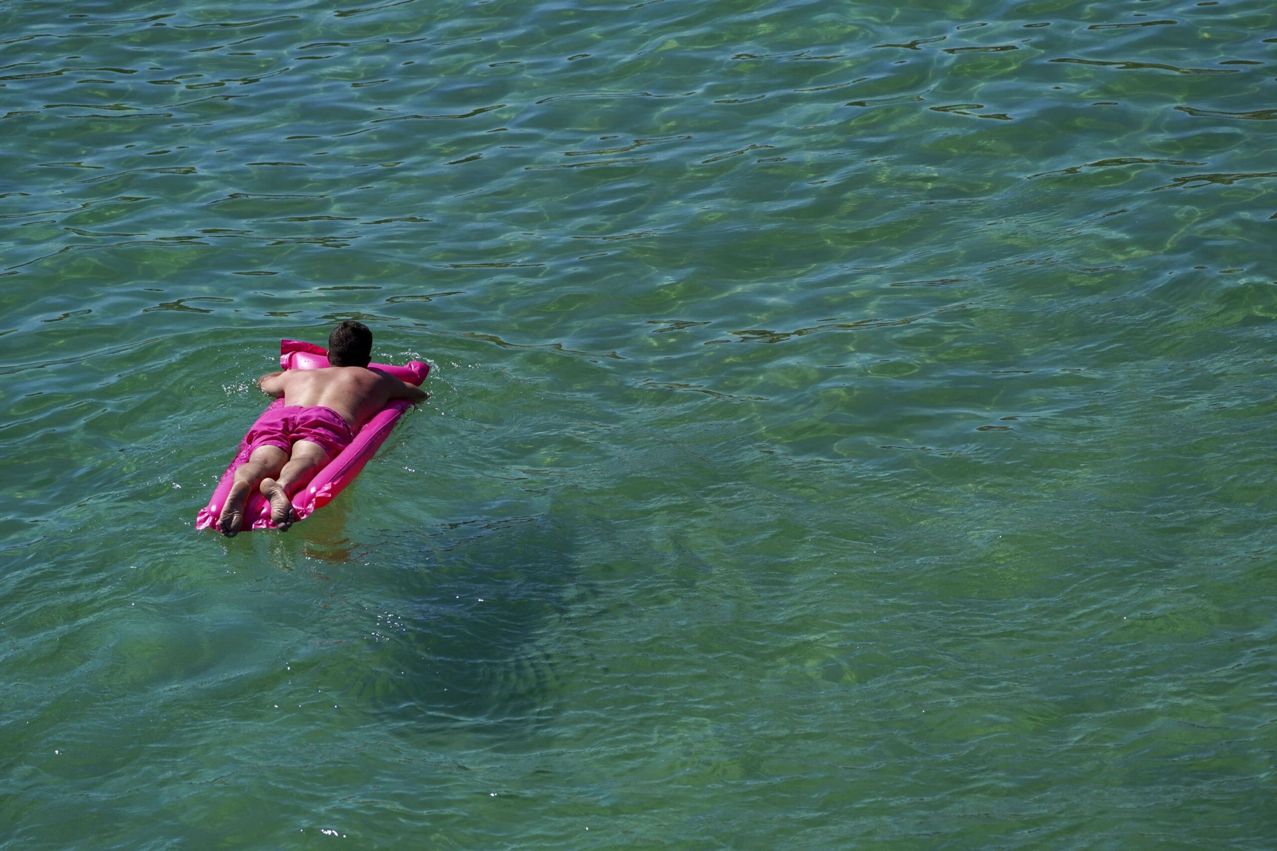 Person lays on pink lilo in the sea  scaled