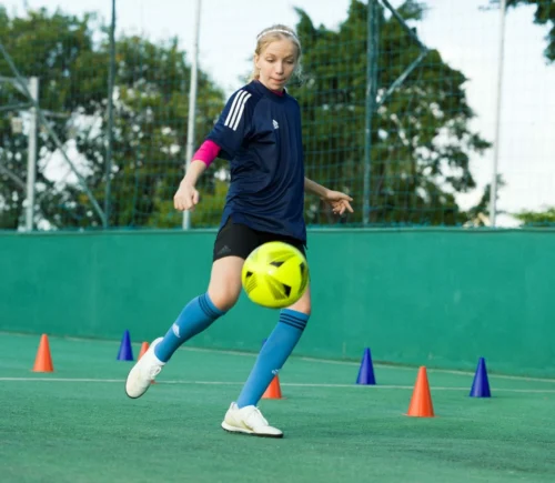 young girl kicks flourescent football scaled e1624564727514