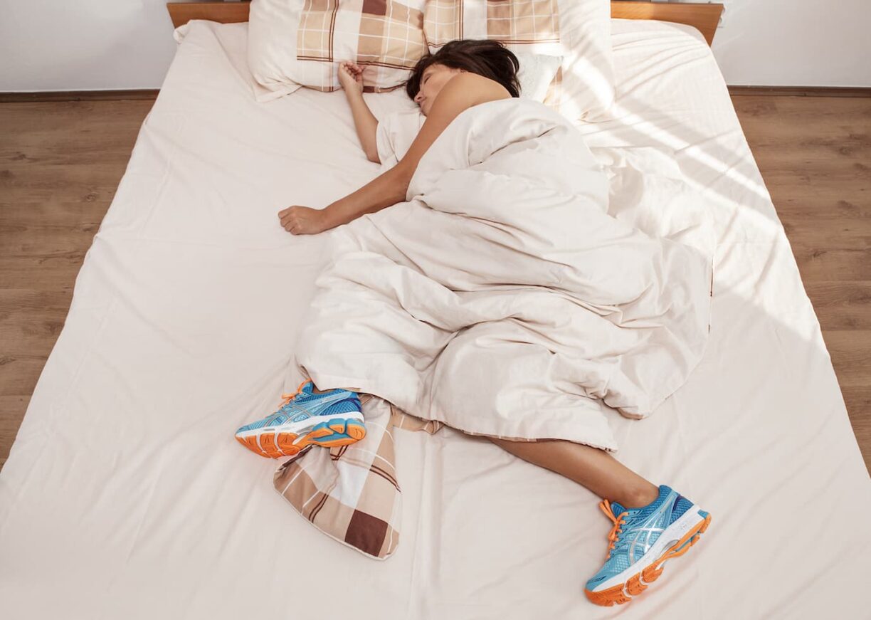 person asleep with running shoes in bed