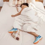 person asleep with running shoes in bed