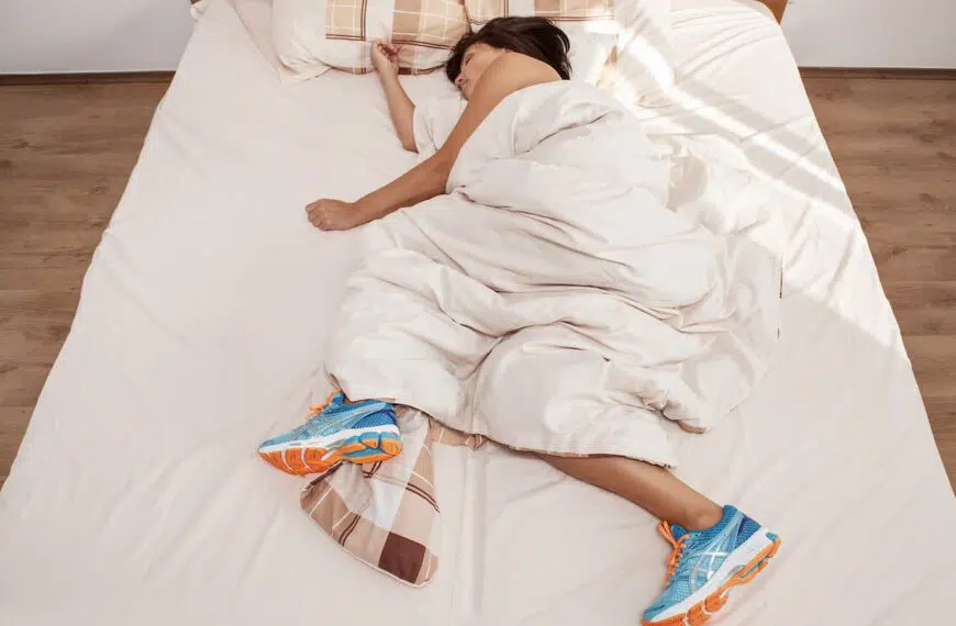 person asleep with running shoes in bed