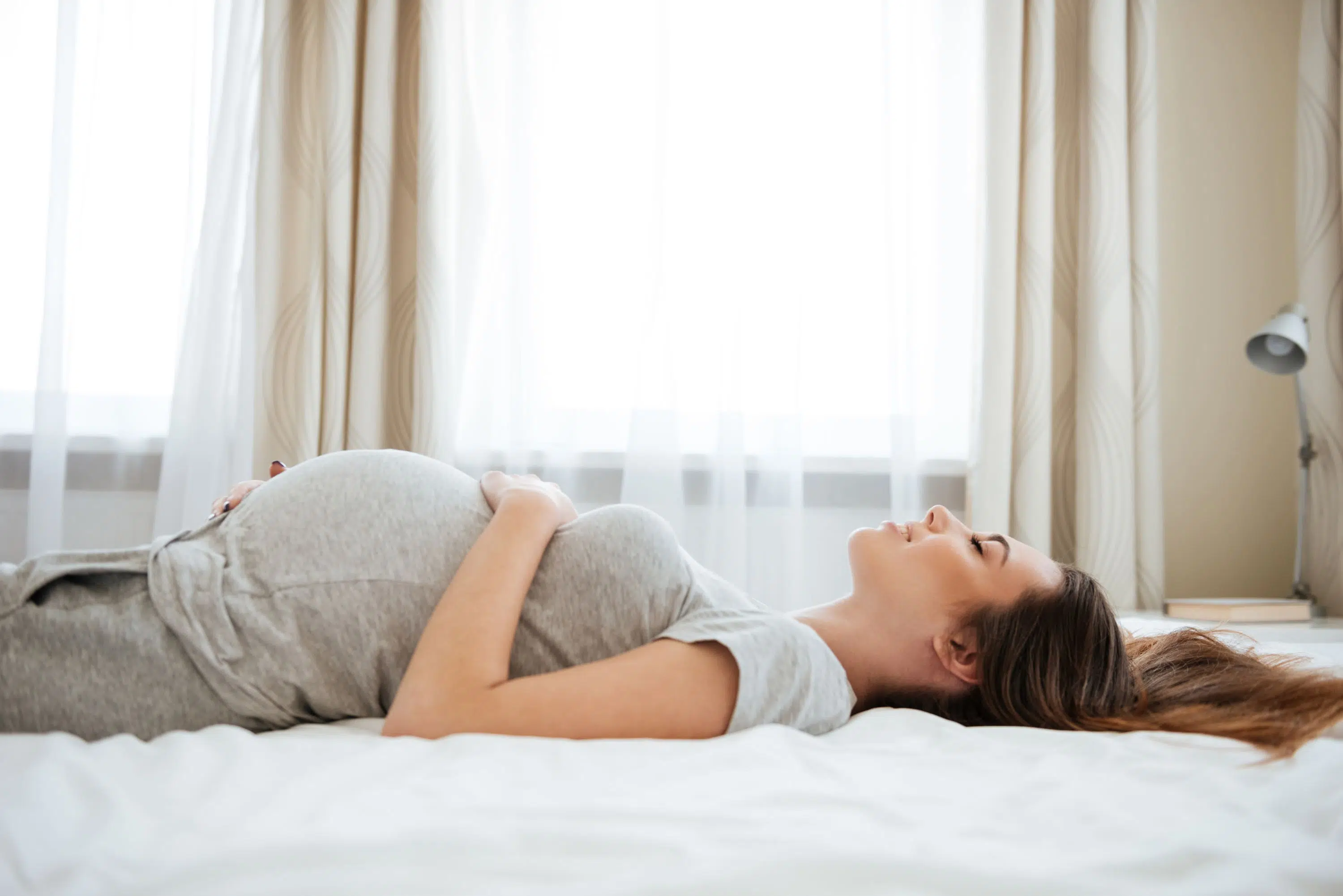 Pregnant woman relaxes on bed scaled