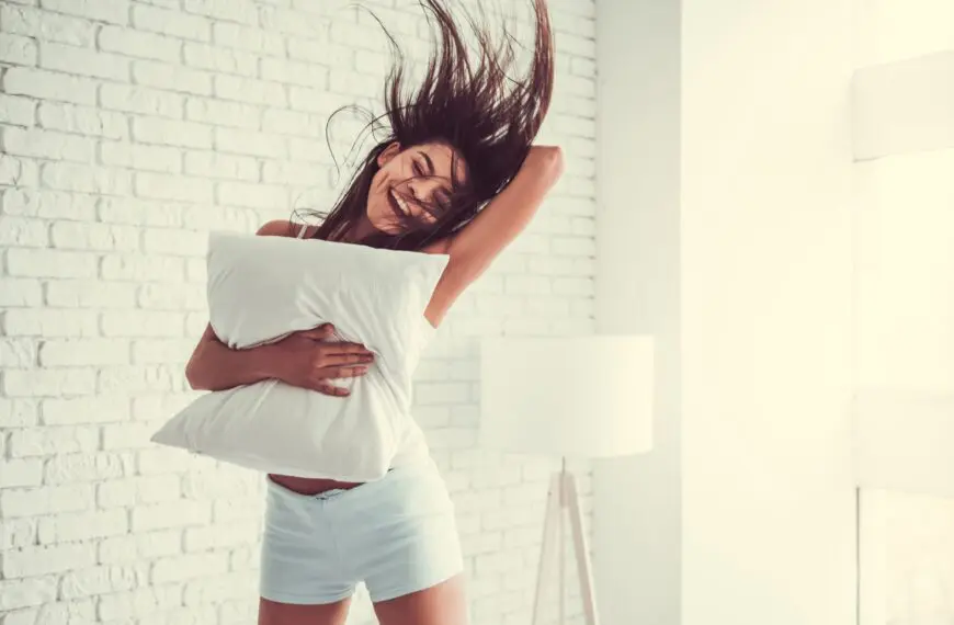 woman jumps in air holding a pillow scaled