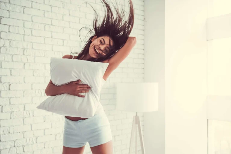 woman jumps in air holding a pillow scaled