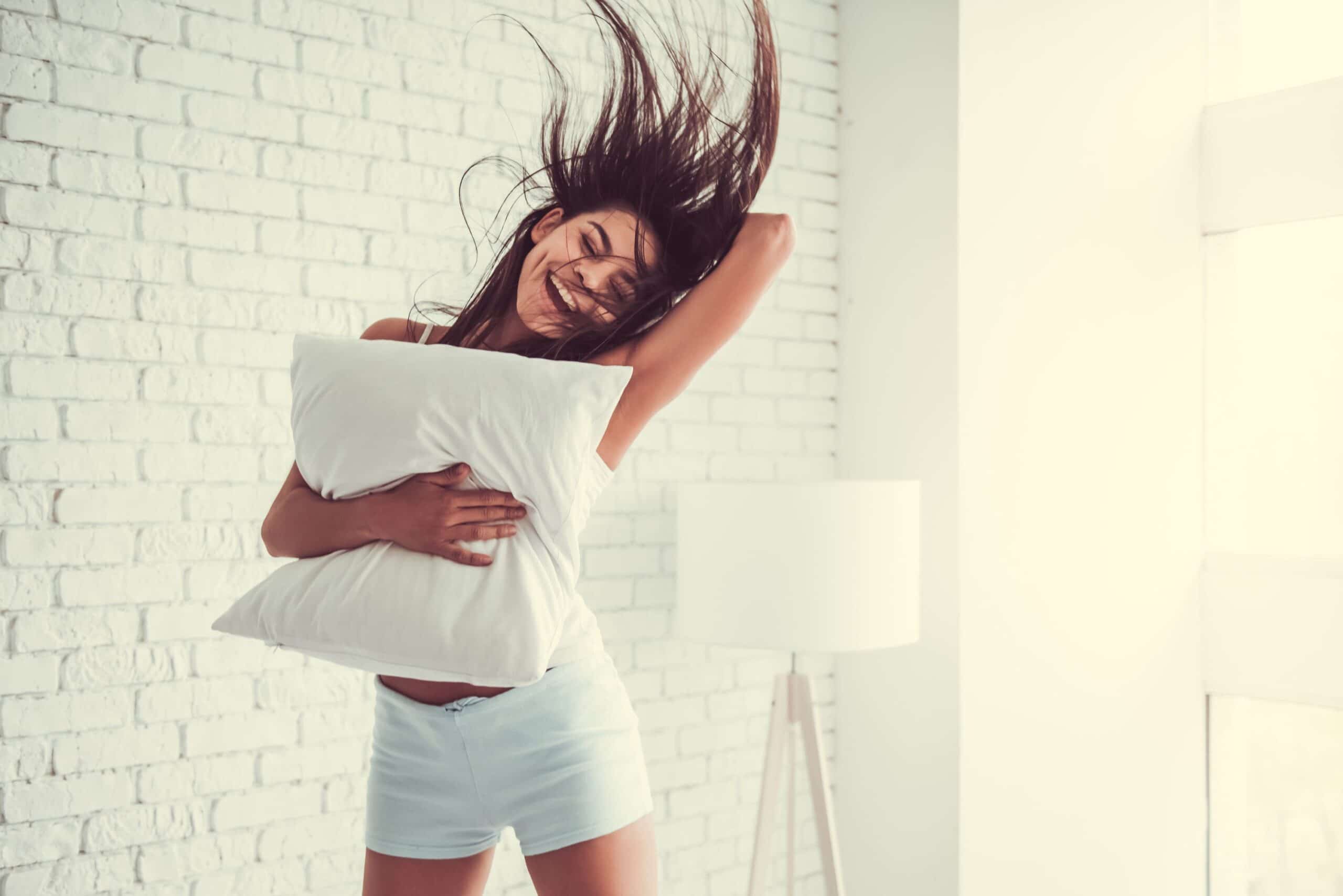 Woman jumps in air holding a pillow scaled