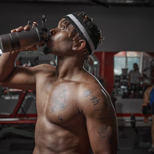 athletic man with naked torso drinking water or sports nutrition from glass after gym workout