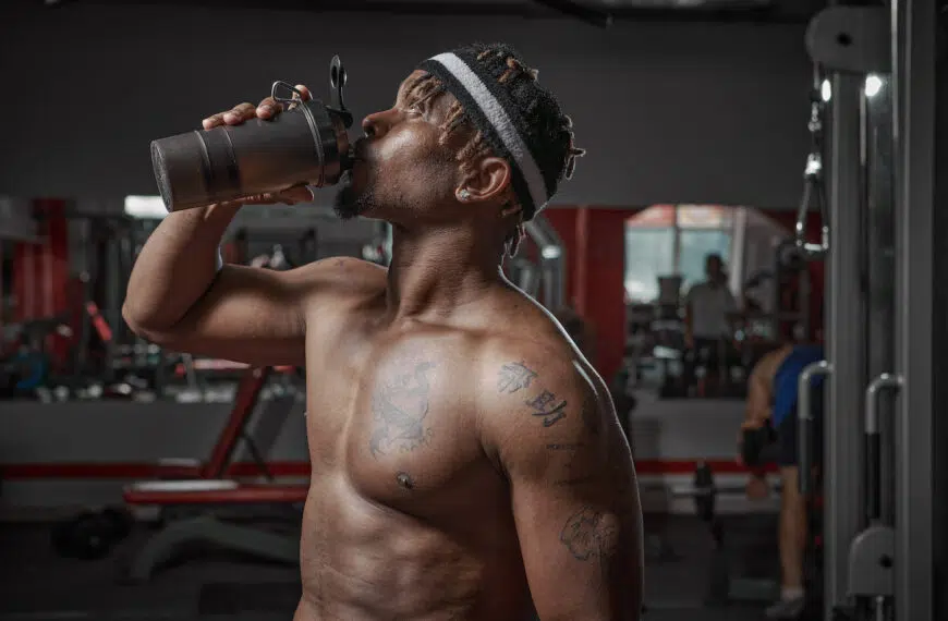 athletic man with naked torso drinking water or sports nutrition from glass after gym workout