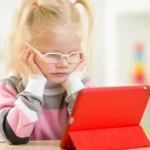 child wearing glasses watches tablet