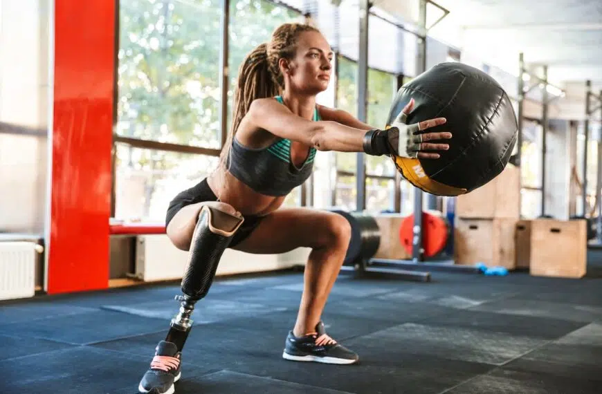 woman with prosthesis in tracksuit doing squats with fitness ball in gym