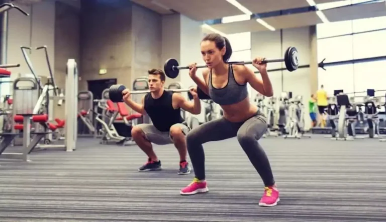 gym couple lift barbells on shoulders