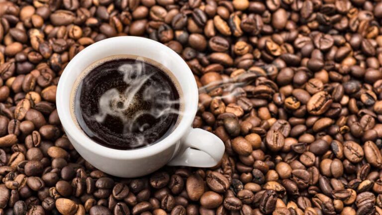 hot coffee in cup surrounded by coffee beans