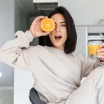woman holds half an orange to her eye