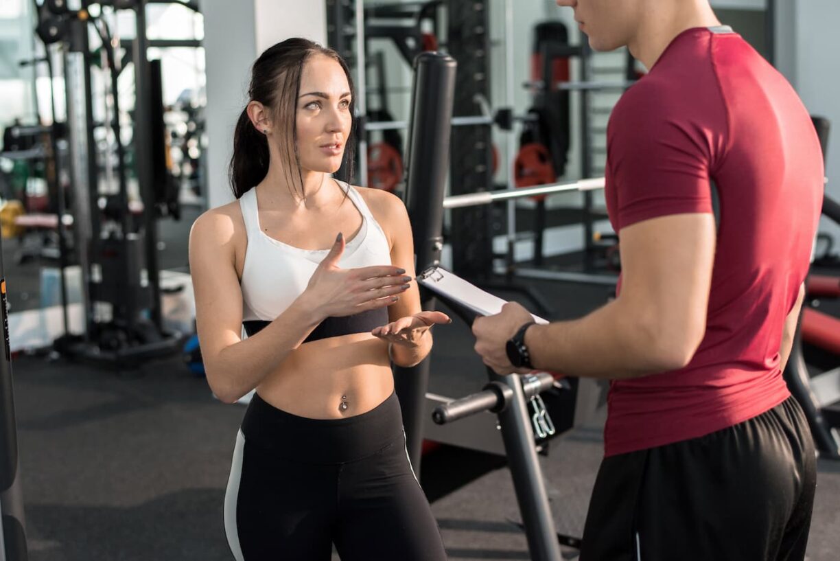 Young woman talking to personal fitness coach in modern gym