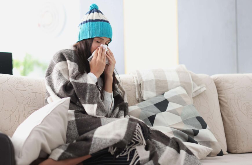 woman blows nose sitting on sofa scaled