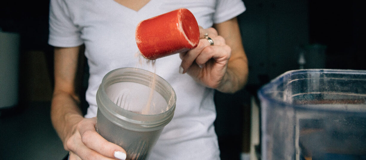 woman puts protein powder into glass