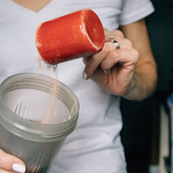 woman puts protein powder into glass