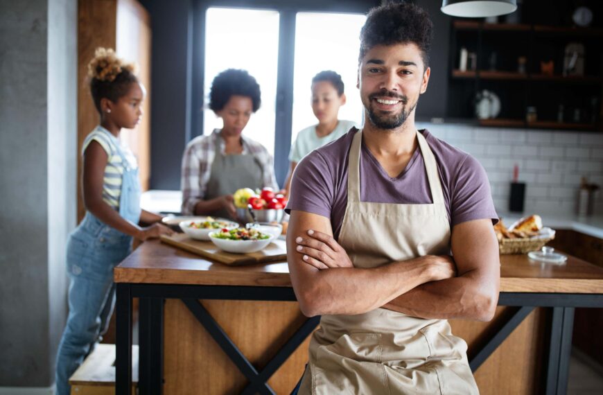 young man smiles in kitchen with family behind him scaled