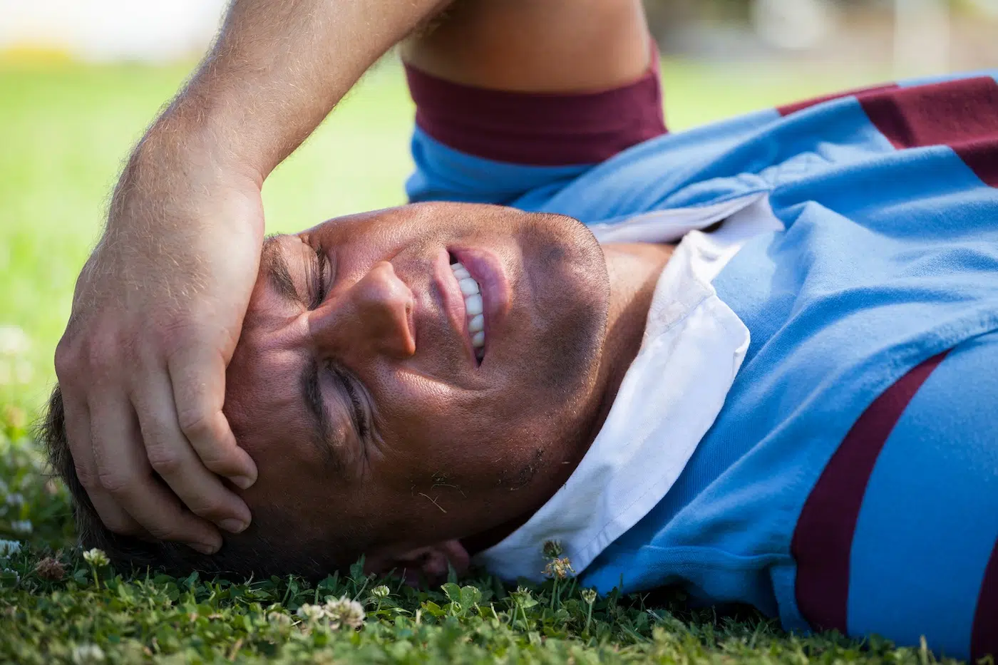 Injured rugby player with eyes closed lying on field