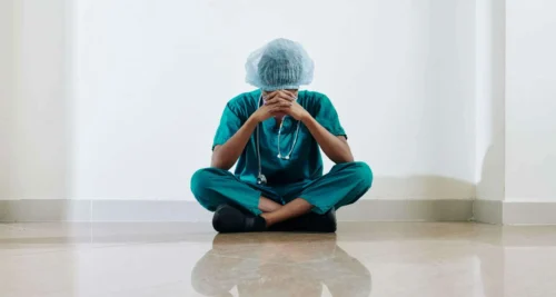 medical professional sits cross legged with head in hands scaled e1638521643776