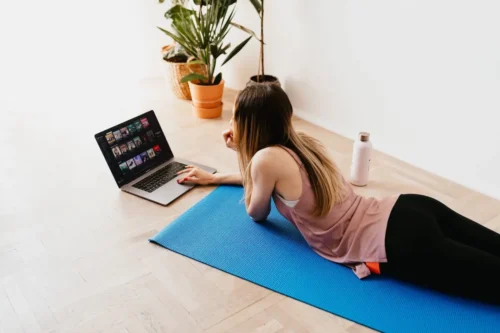 woman on yoga mat watching video on laptop